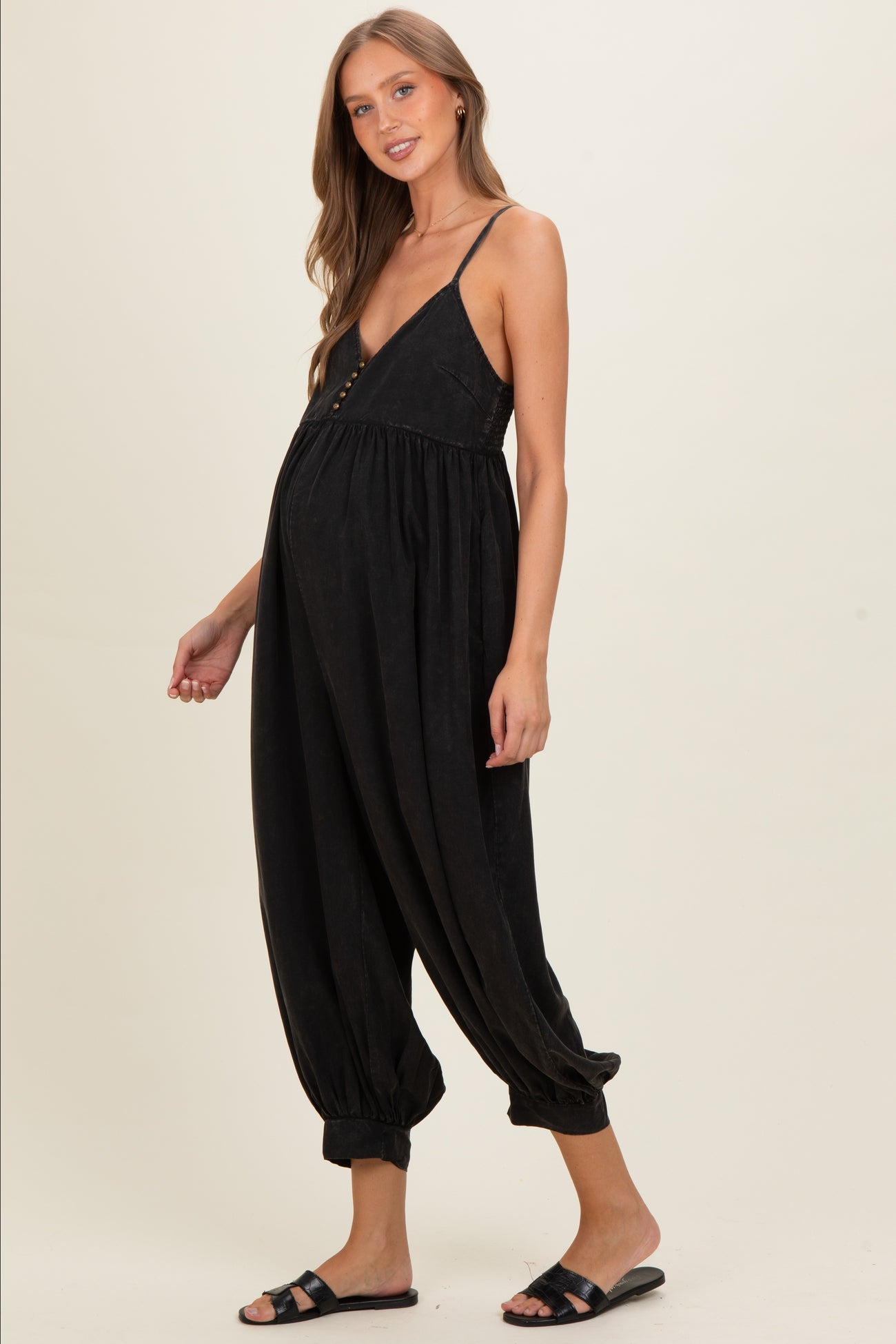 woman wearing a black maternity jumpsuit with a deep v-neck and adjustable straps, showing her baby bump