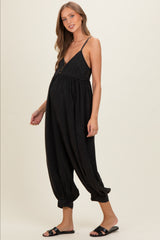 woman wearing a black maternity jumpsuit with a deep v-neck and adjustable straps, showing her baby bump
