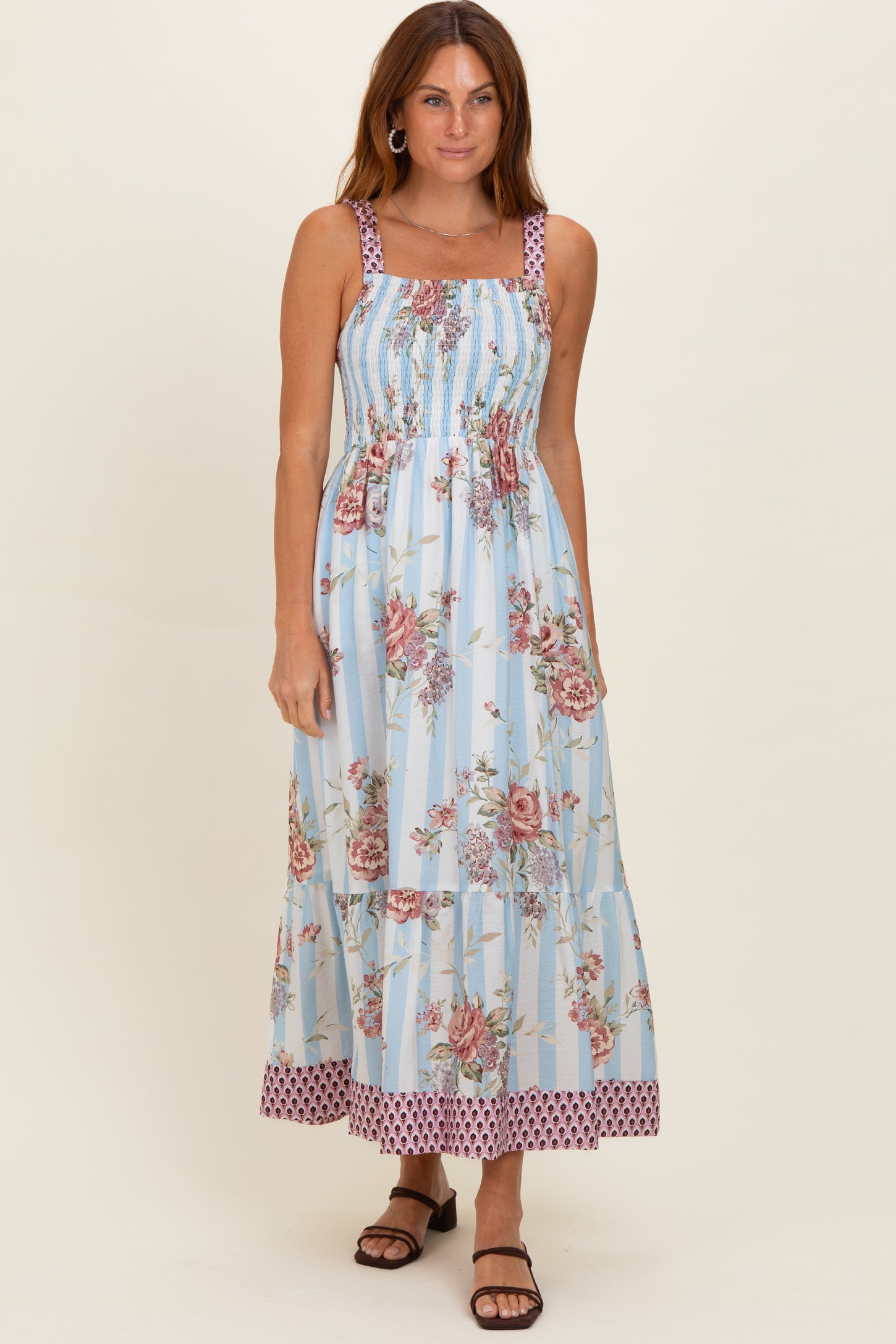 woman wearing a blue floral maxi dress with smocked bodice and patterned hem, posing with a natural expression