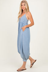 woman wearing a light blue denim jumpsuit with spaghetti straps and side pockets, paired with flat sandals