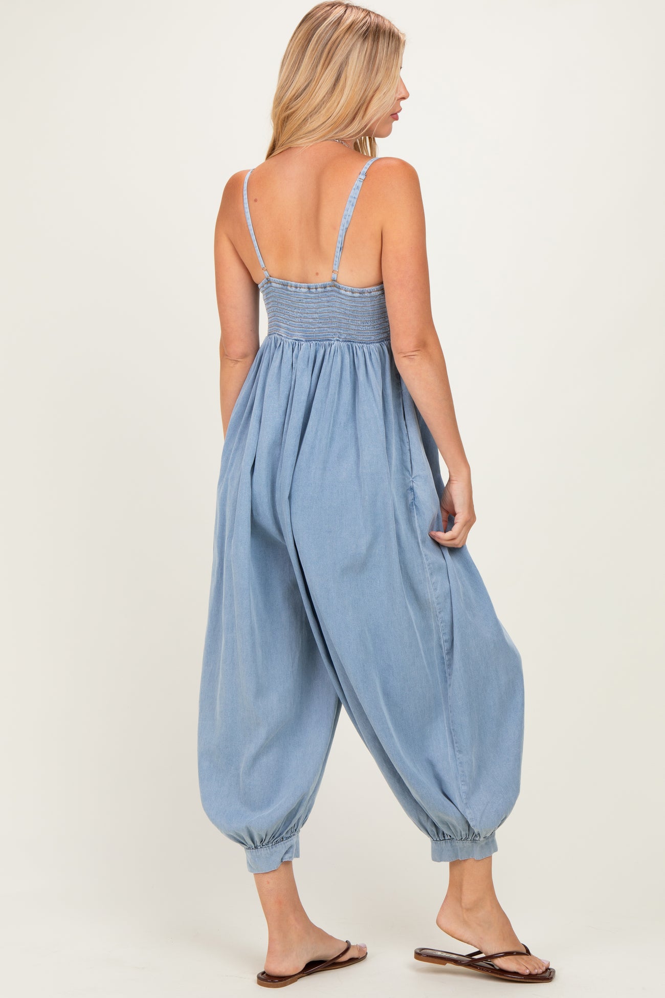 woman wearing a light blue denim jumpsuit with spaghetti straps and tapered balloon legs