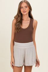 woman wearing a brown maternity tank top and light beige shorts, showcasing a relaxed style with a baby bump visible