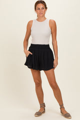 woman wearing a fitted white sleeveless top and black drawstring shorts, posing with hands in pockets