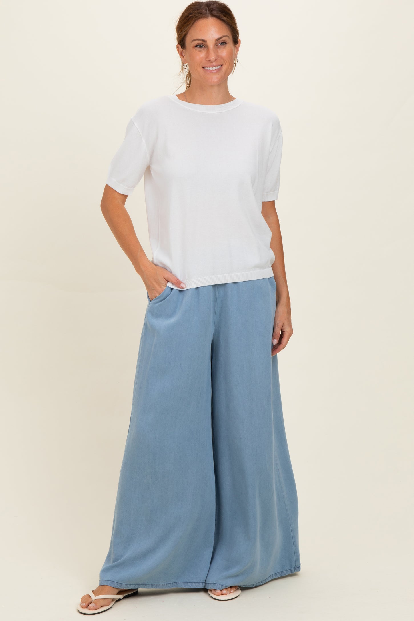 woman wearing a white short sleeve top and light blue wide-leg pants, standing with one hand in pocket