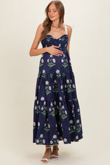 woman wearing a navy blue floral print maternity maxi dress with smocked bodice and adjustable straps, holding her baby bump