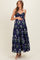 woman wearing a navy blue floral print maternity maxi dress with smocked bodice and adjustable straps, holding her baby bump