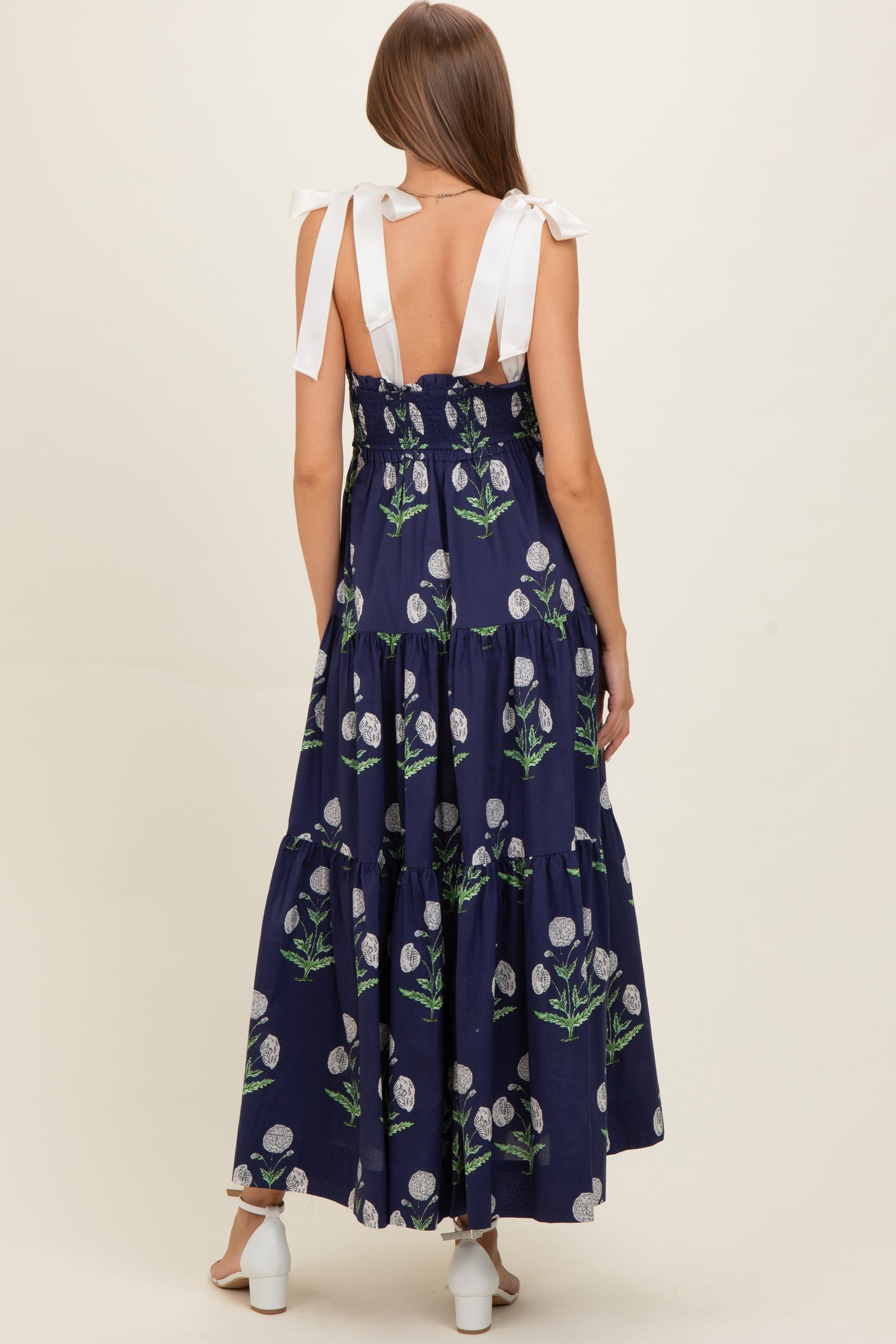 woman wearing a navy blue floral print maternity maxi dress with bow-tie straps and a tiered skirt, showcasing her baby bump