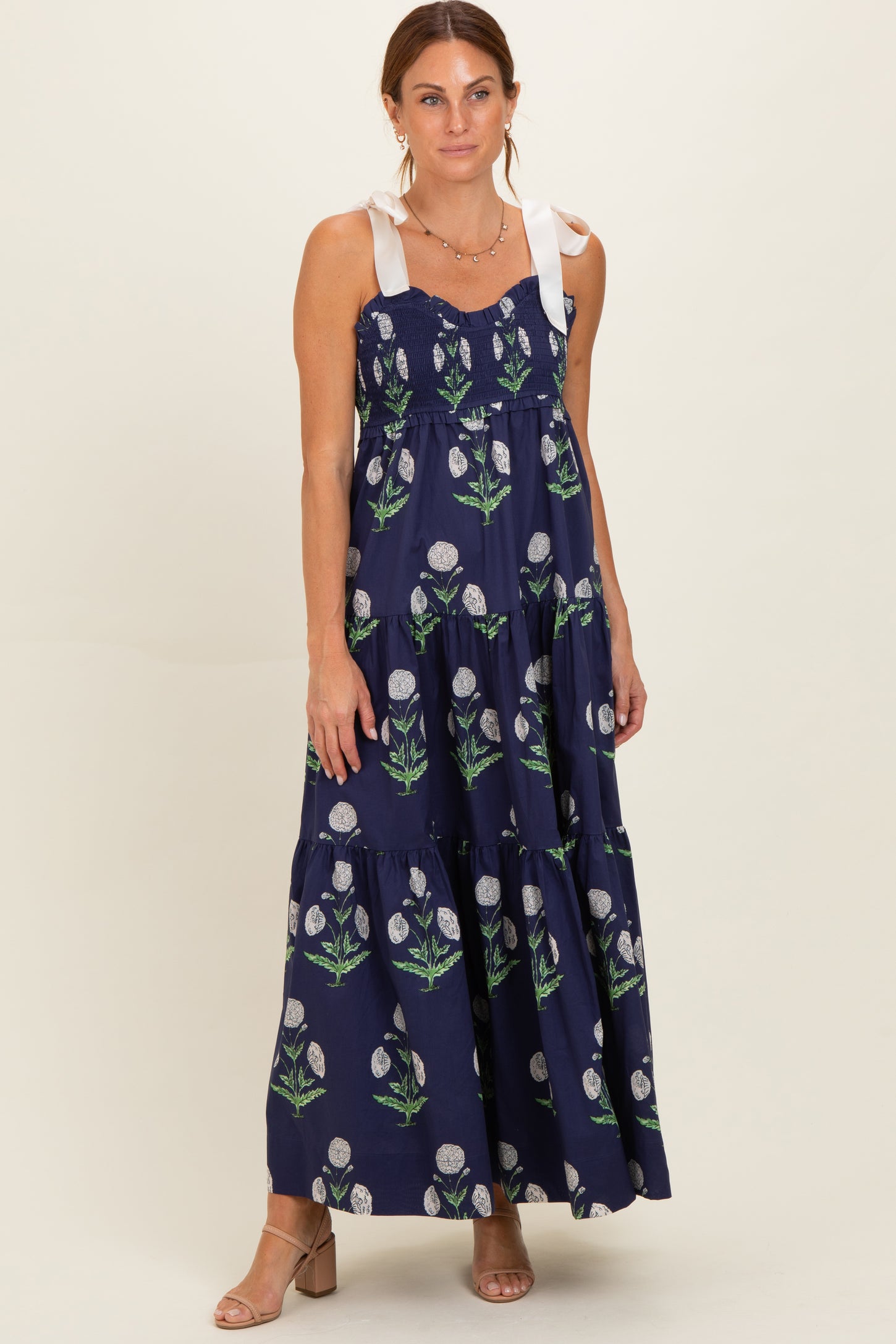 woman wearing a navy floral maxi dress with tie shoulder straps and a tiered skirt