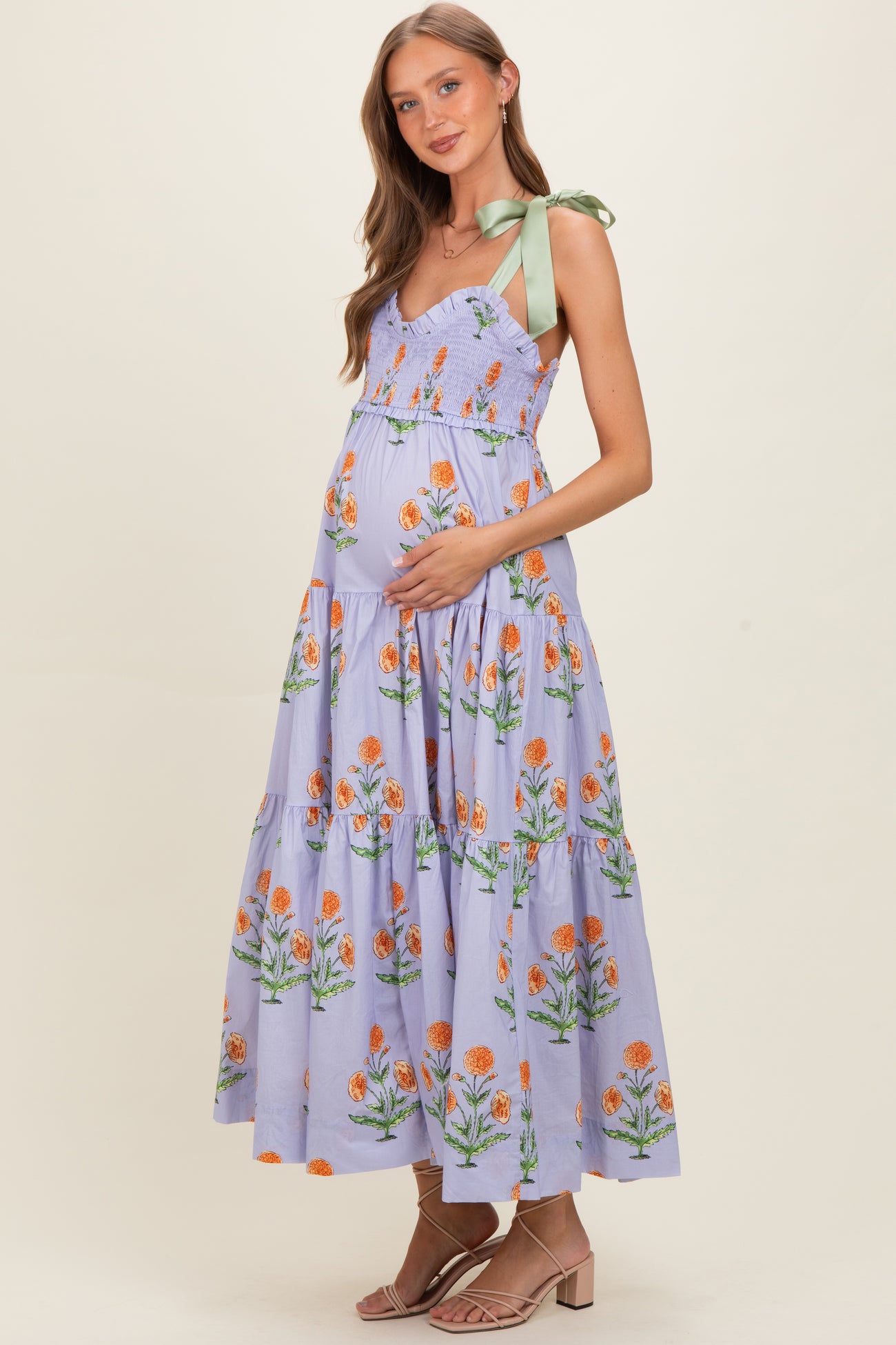 woman wearing a lavender floral maternity maxi dress with adjustable green ribbon straps and a visible baby bump