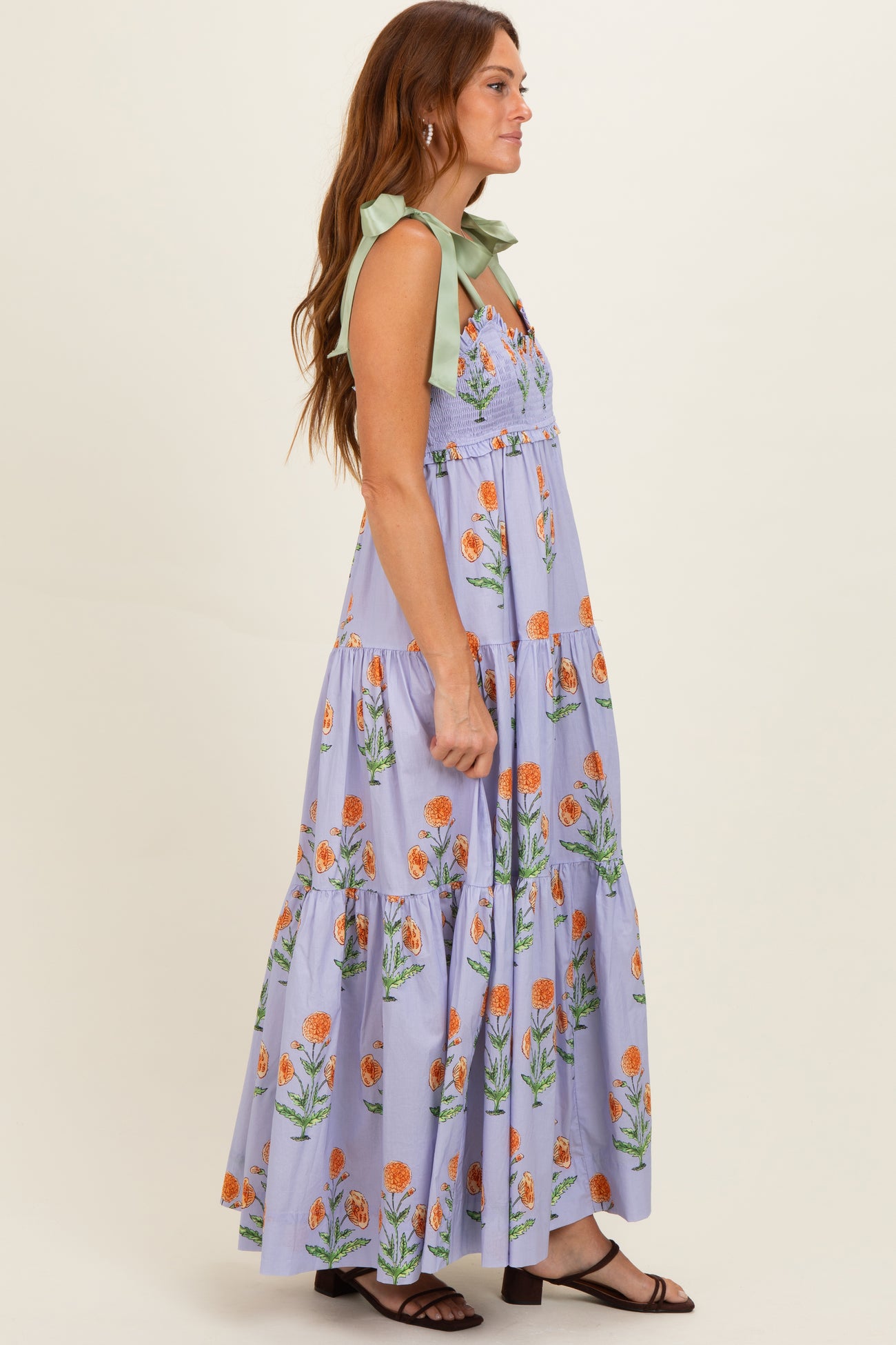 woman wearing a lavender floral maxi dress with green tie straps and a tiered skirt