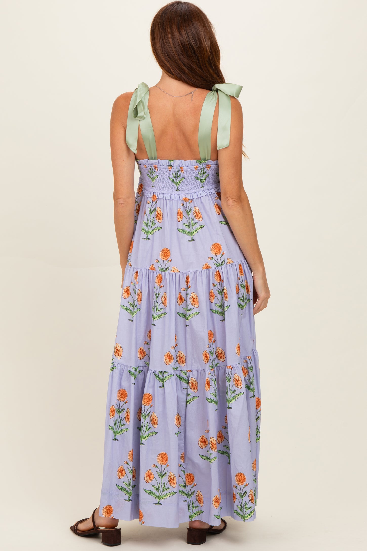 woman wearing a purple floral maxi dress with green tie straps, showing tiered design and back details