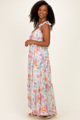 woman wearing a flowy maxi dress with colorful floral prints and ruffled straps, standing sideways against a light background