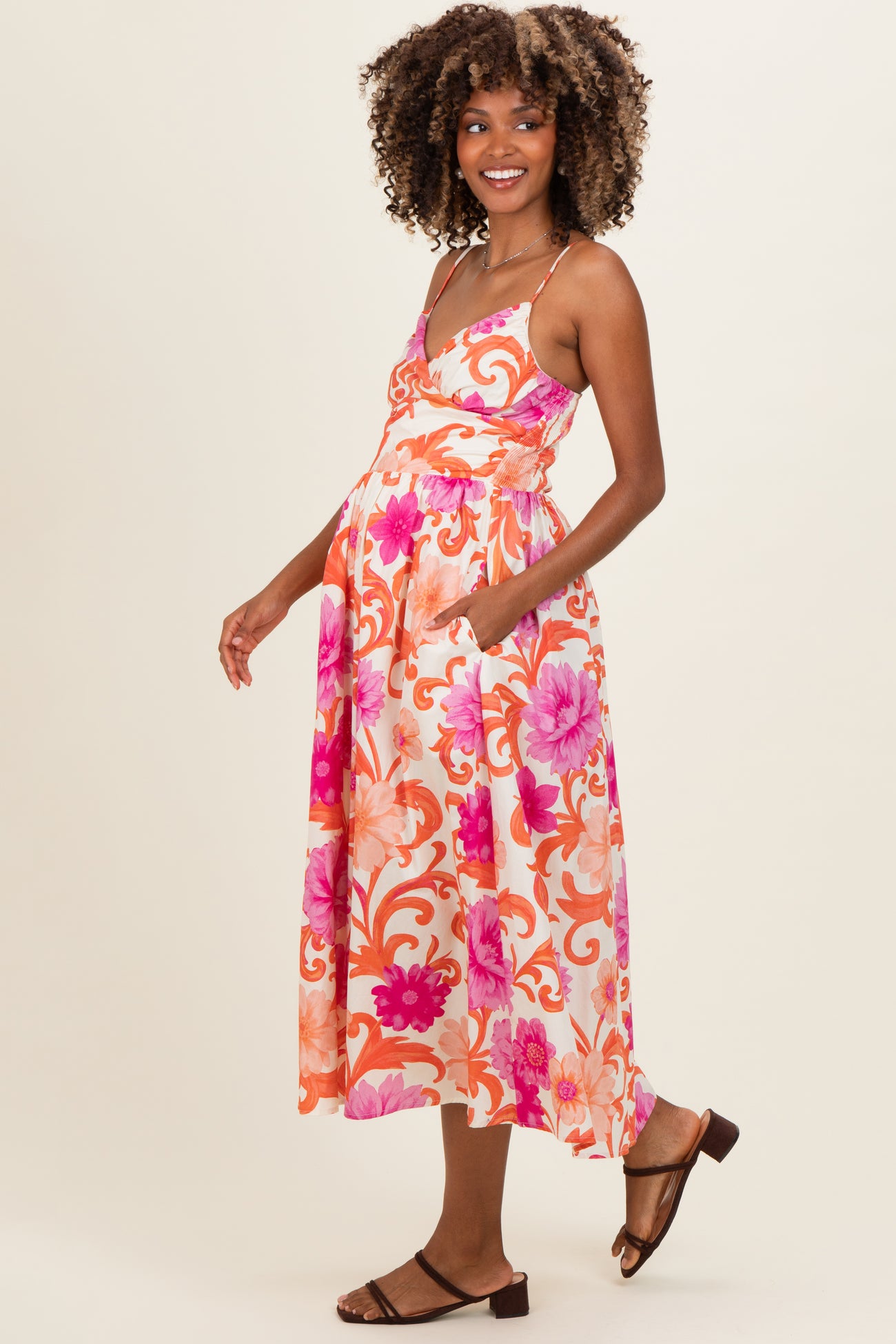 woman wearing a floral pink and orange maternity maxi dress, showing her baby bump with pockets and a relaxed fit
