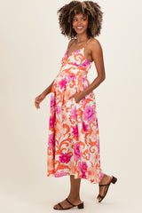 woman wearing a floral pink and orange maternity maxi dress, showing her baby bump with pockets and a relaxed fit