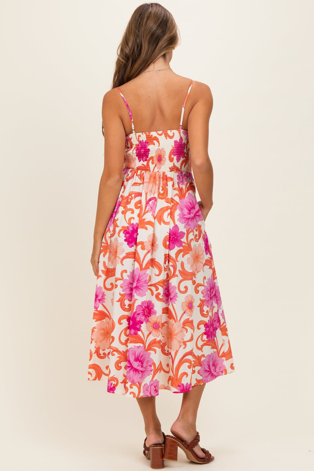 woman wearing a back view of a floral print midi dress with spaghetti straps and smocked bodice in pink and orange tones