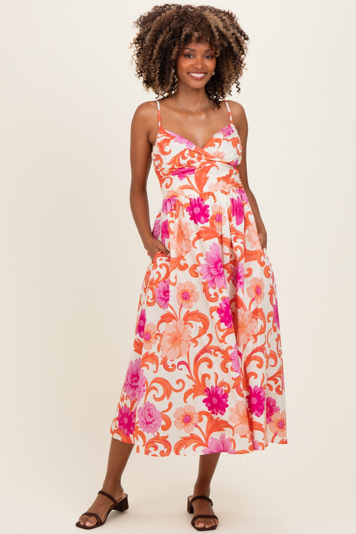 woman wearing a floral print maternity dress with spaghetti straps and pockets, showcasing her baby bump