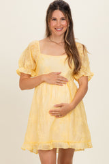 woman wearing a yellow maternity dress with puff sleeves and holding her baby bump