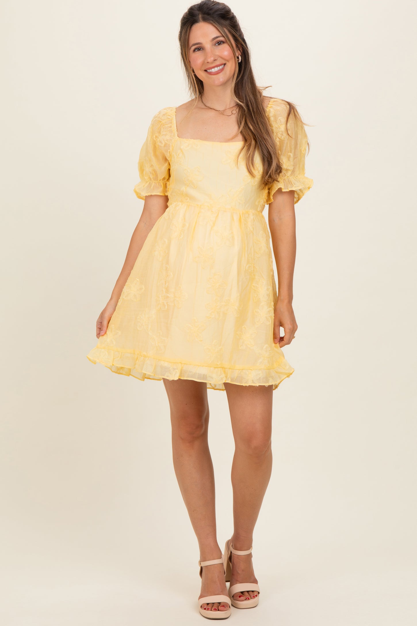 woman wearing a yellow short puff sleeve maternity dress with a square neckline and ruffled hem