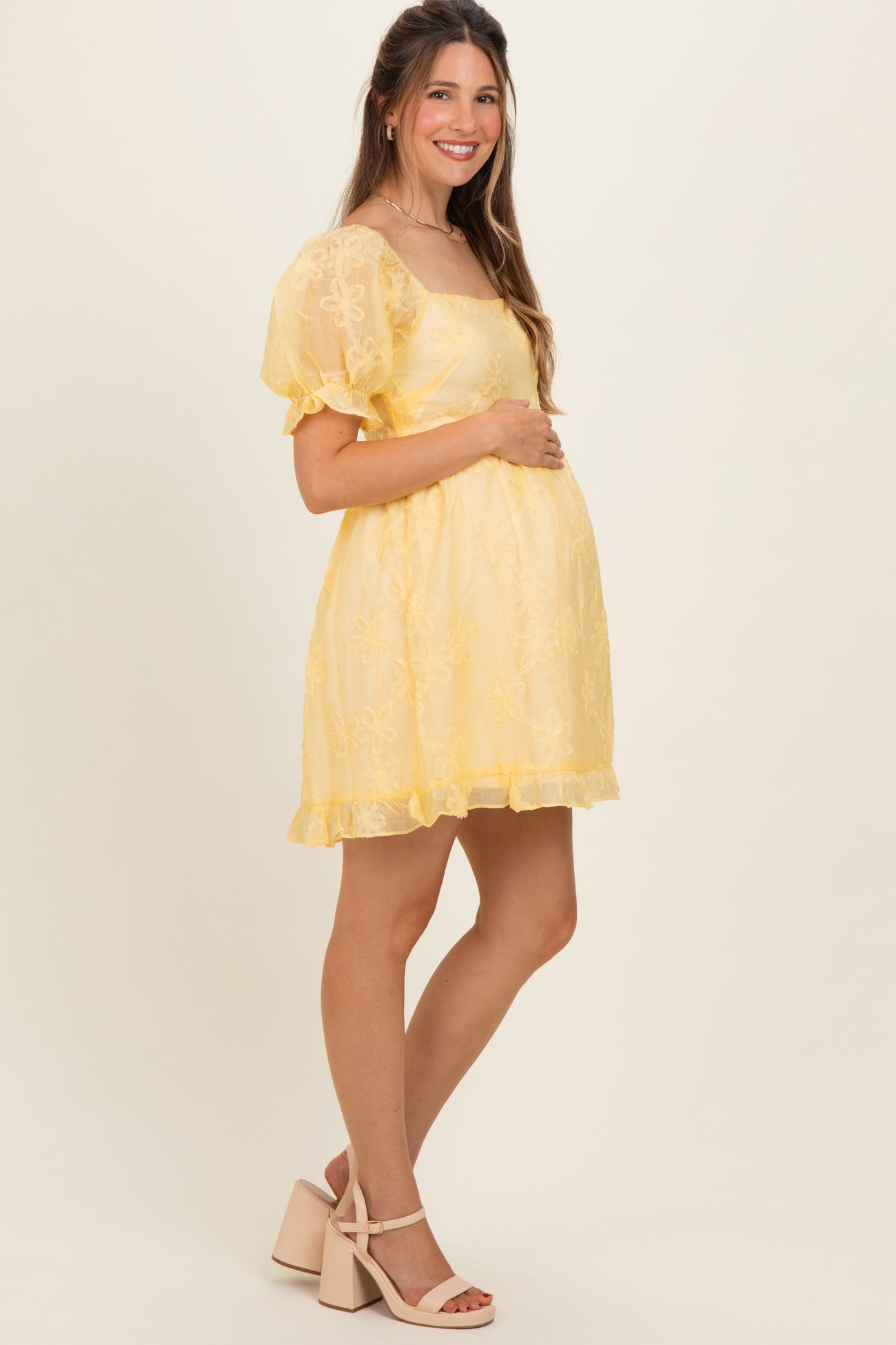 woman wearing a yellow maternity dress with puff sleeves and floral embroidery, showing her baby bump