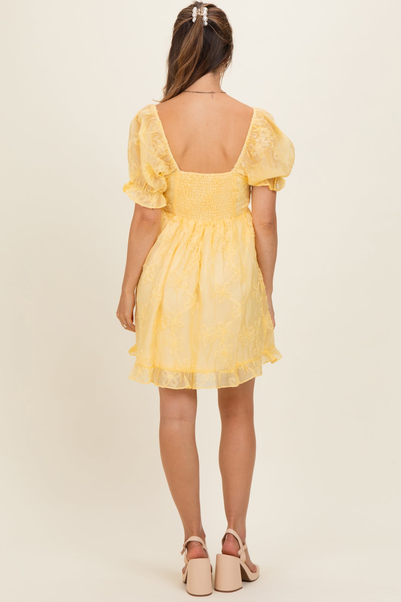 woman wearing a yellow puff sleeve maternity dress with a smocked back and ruffled hem, showing a baby bump