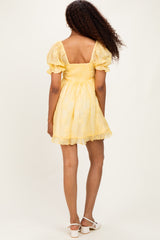 woman wearing a yellow short puff sleeve dress with a smocked back and lace details