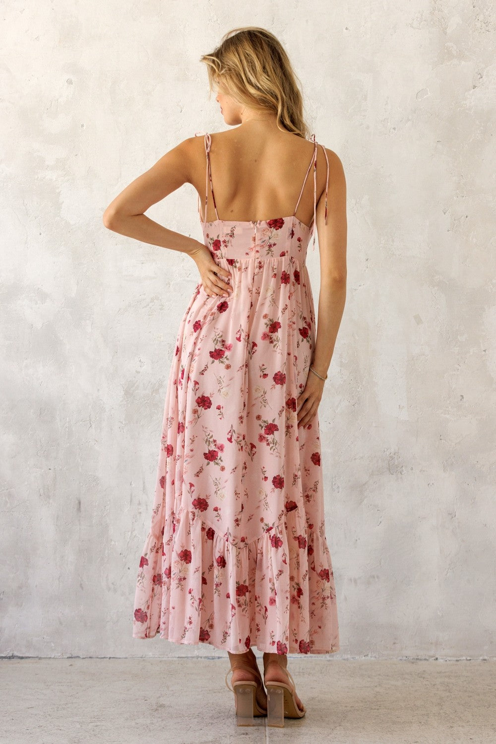 woman wearing a pink floral maxi dress with adjustable straps and a ruffled hem, viewed from the back