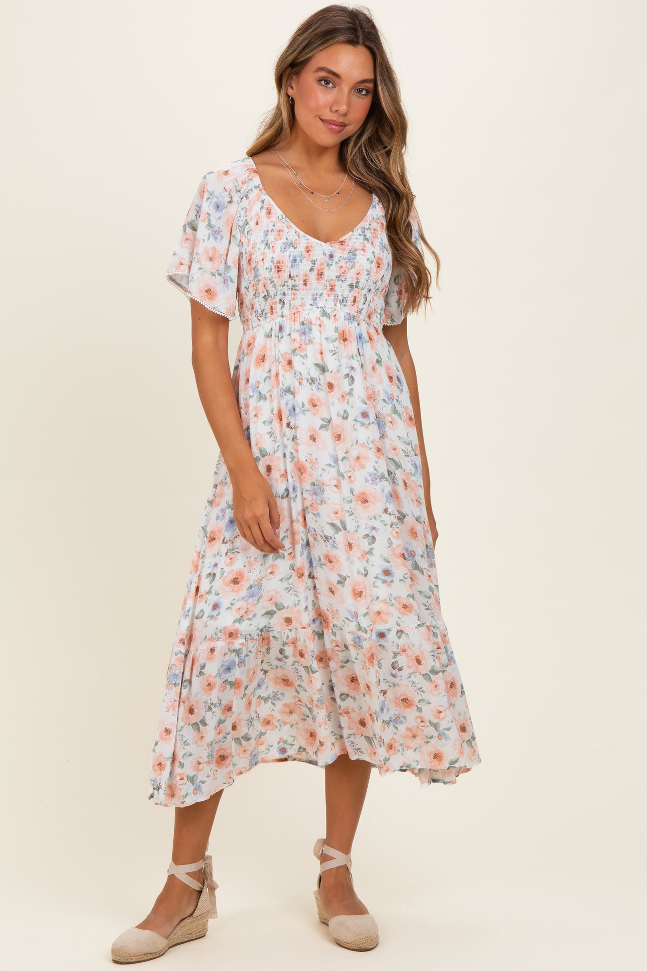 woman wearing a blush floral midi dress with short sleeves and a smocked bodice, standing against a neutral background