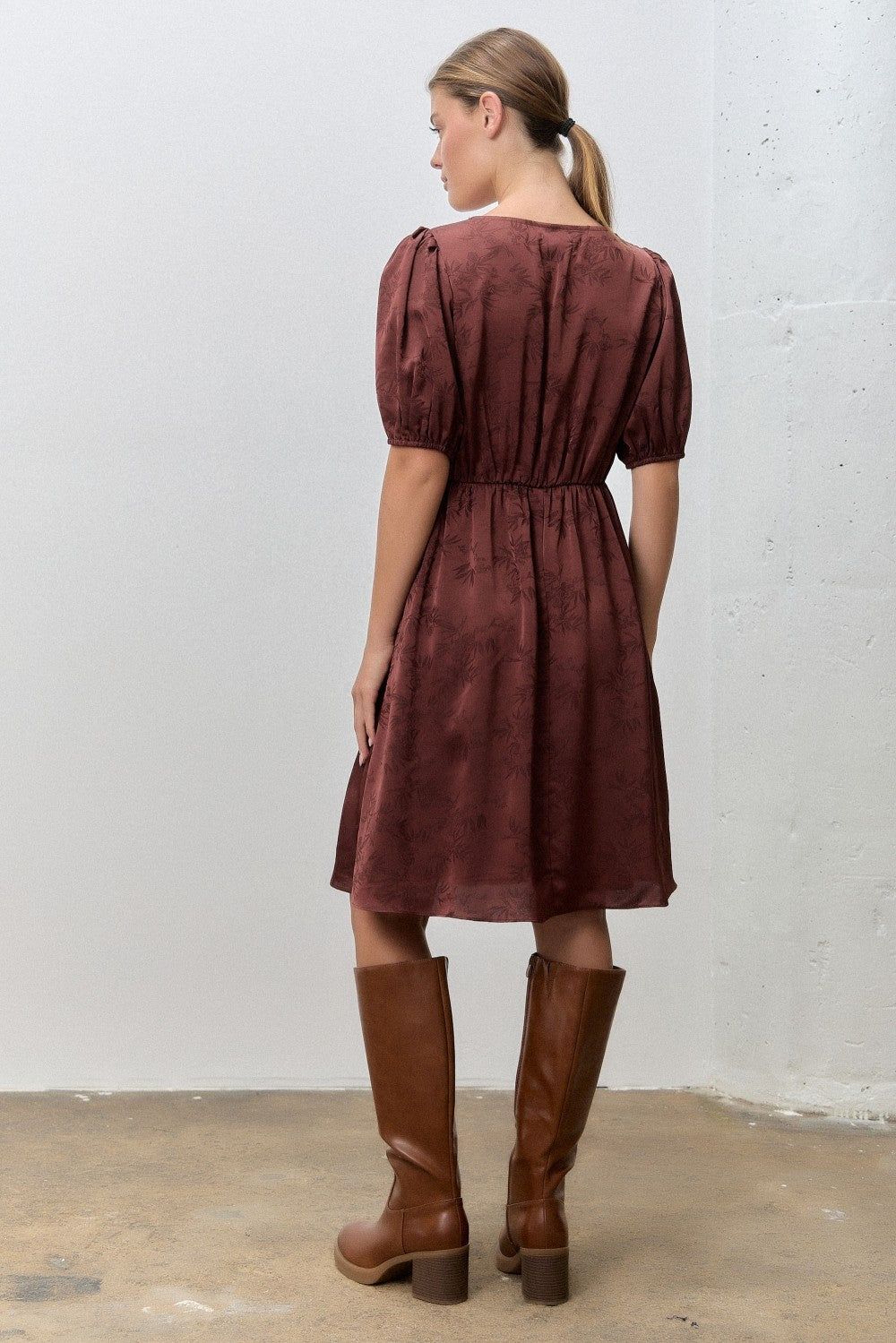 woman wearing a burgundy short sleeve dress with a smocked waist and puff sleeves, paired with knee-high brown boots