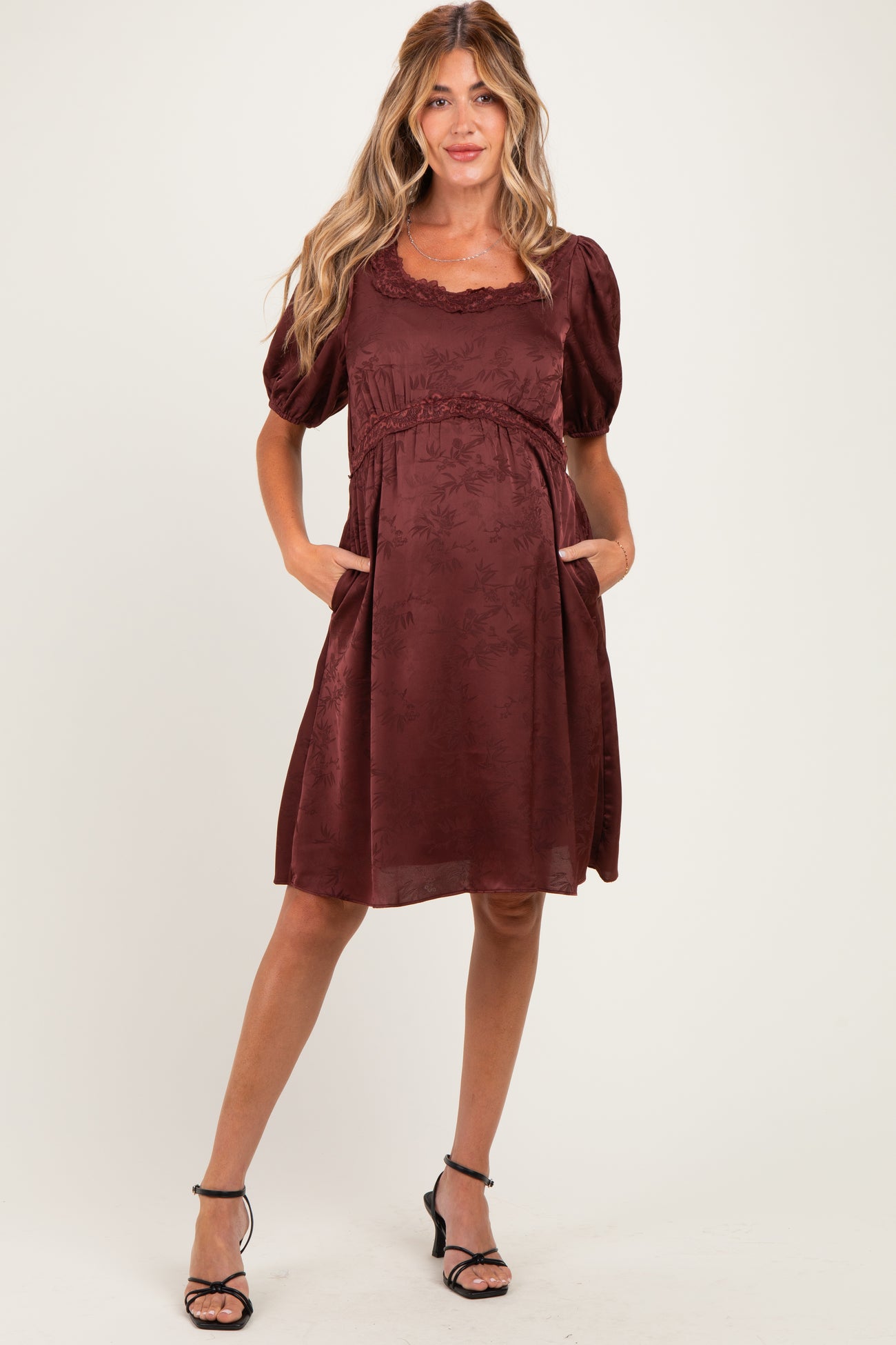 woman wearing a burgundy maternity dress with puff sleeves and pockets, showcasing a baby bump