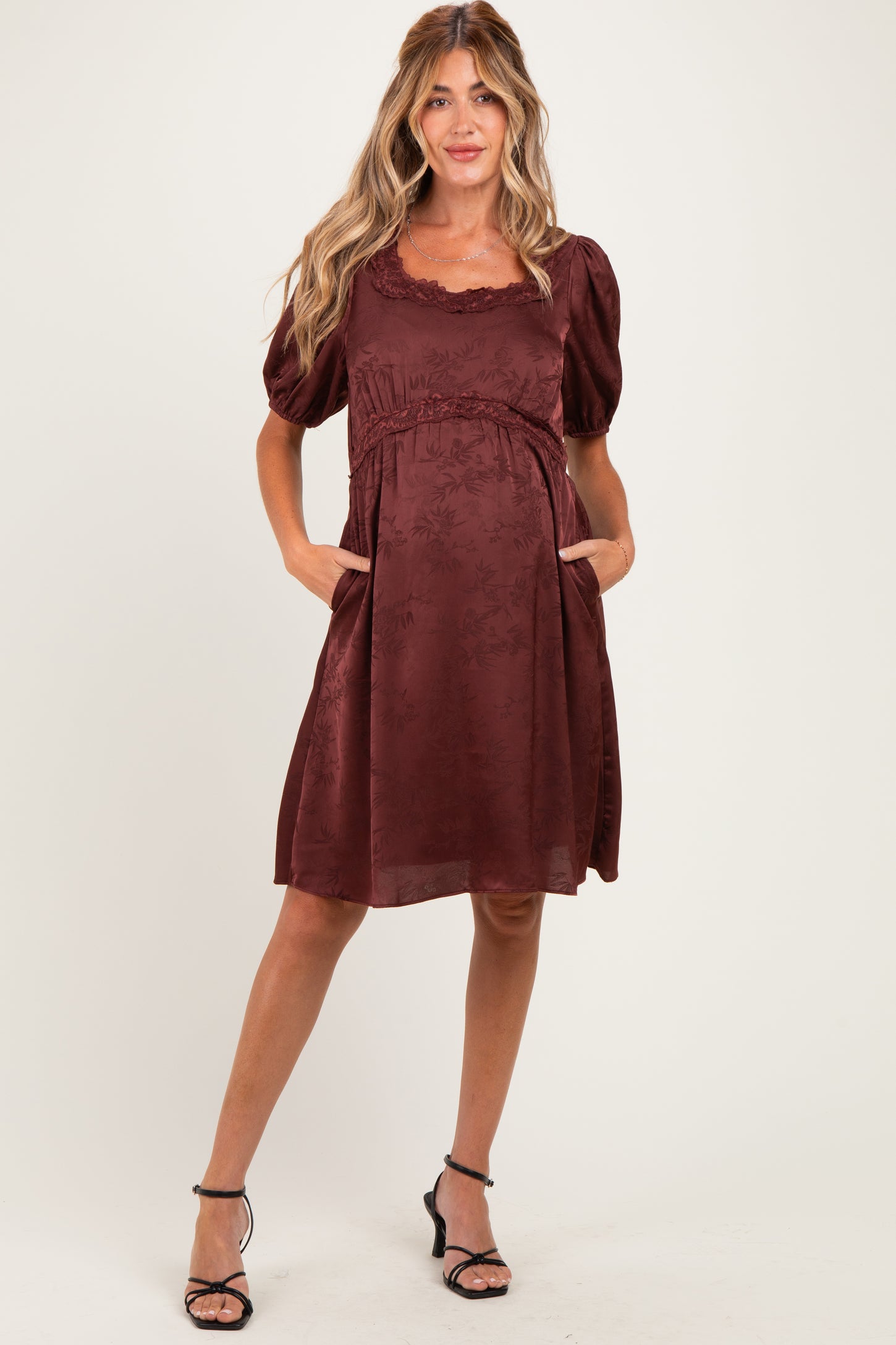 woman wearing a burgundy maternity dress with puff sleeves and pockets, showcasing a baby bump