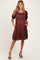 woman wearing a burgundy maternity dress with puff sleeves and pockets, showcasing a baby bump