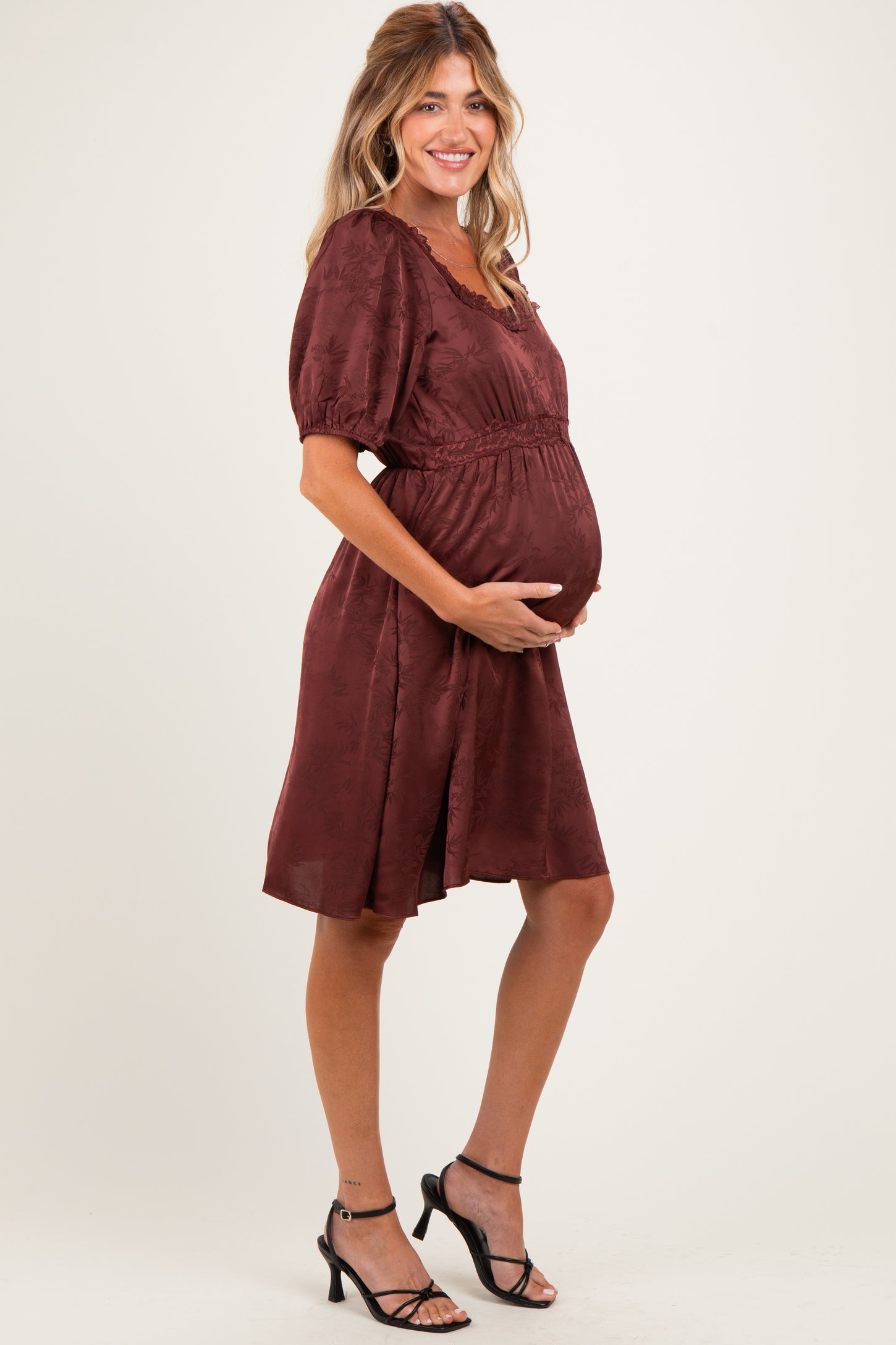 woman wearing a burgundy short sleeve maternity dress with a cinched waist and holding her baby bump