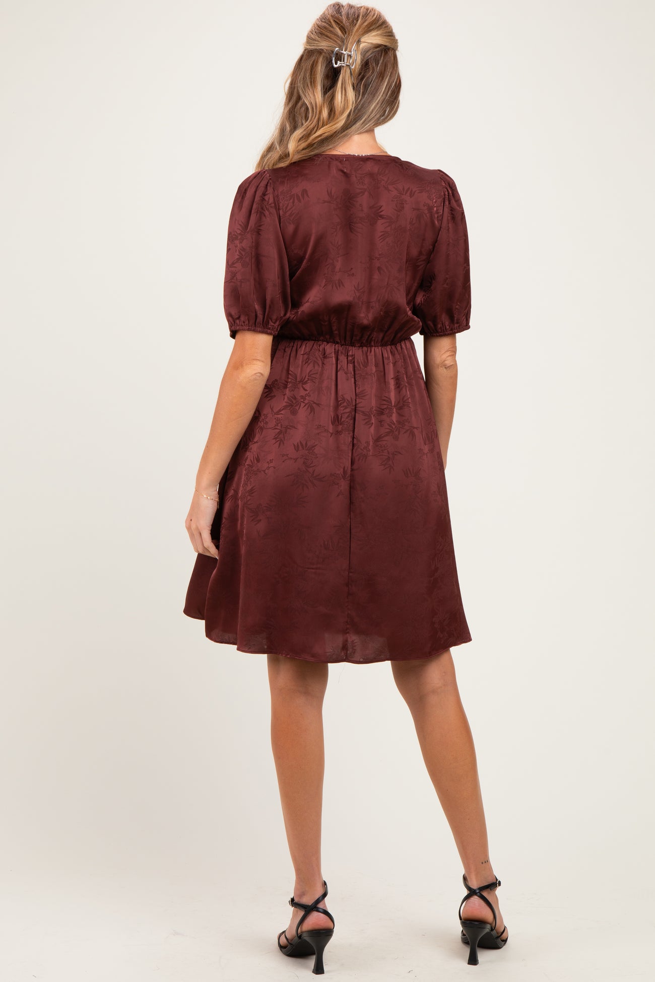woman wearing a burgundy short sleeve maternity dress with a fitted waist and a flowy skirt, shown from the back