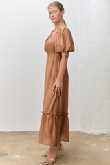 woman wearing a brown puff sleeve maxi dress with a fitted waist and ruffled hem, standing in a side profile