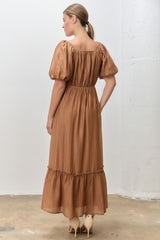 woman wearing a backview of a rust-colored maxi dress with puff sleeves and a tiered skirt