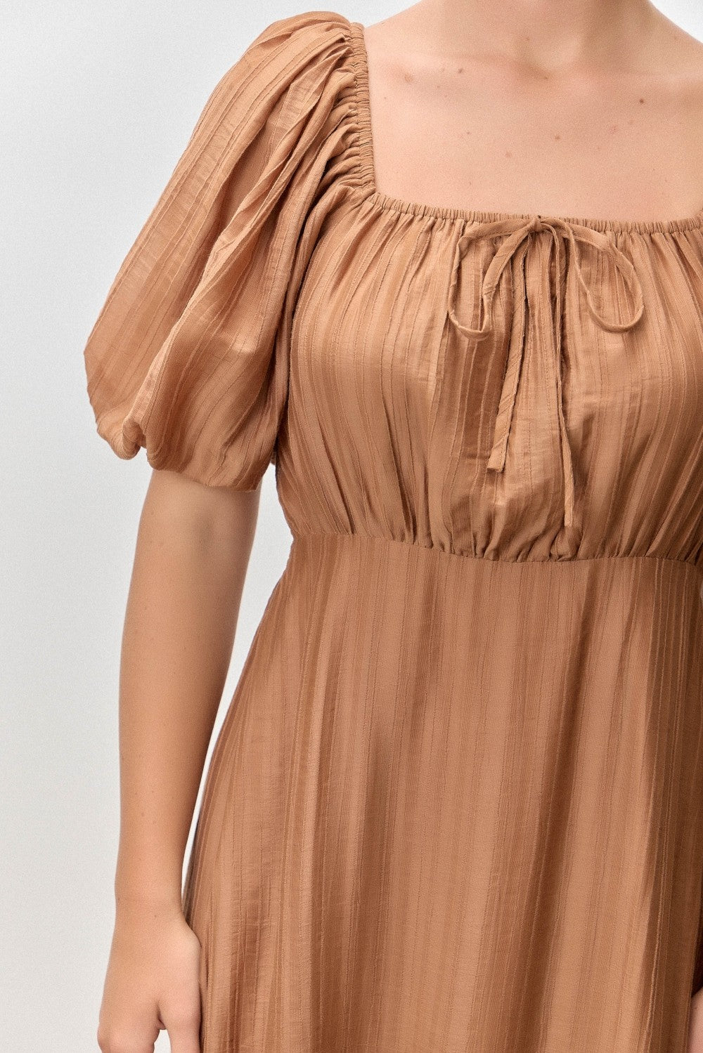 woman wearing a brown puff sleeve dress with a square neckline and tie detail