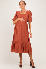 woman wearing a rust-colored short sleeve maternity dress with a square neckline and tiered skirt, holding her baby bump