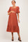 woman wearing a rust-colored short sleeve maternity dress with a square neckline and tiered skirt, holding her baby bump