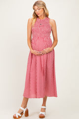 woman wearing a red and white gingham maternity dress with a smocked bodice and holding her baby bump