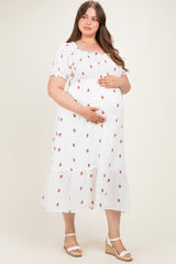woman wearing a white maternity plus dress with floral print and ruffle hem, gently cradling her baby bump