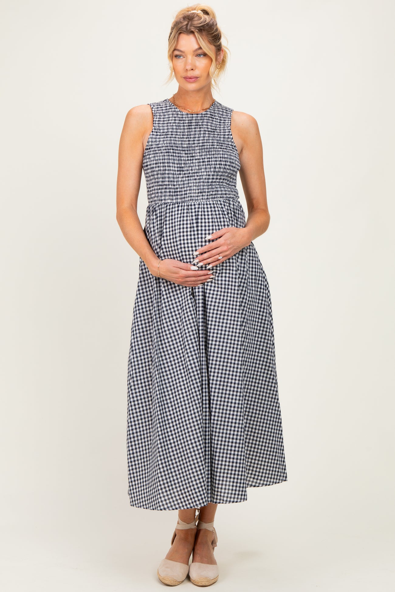 woman wearing a black and white gingham maternity dress with a smocked bodice and holding her baby bump