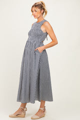 woman wearing a navy and white gingham maternity dress with smocked bodice and side pockets, showing her baby bump