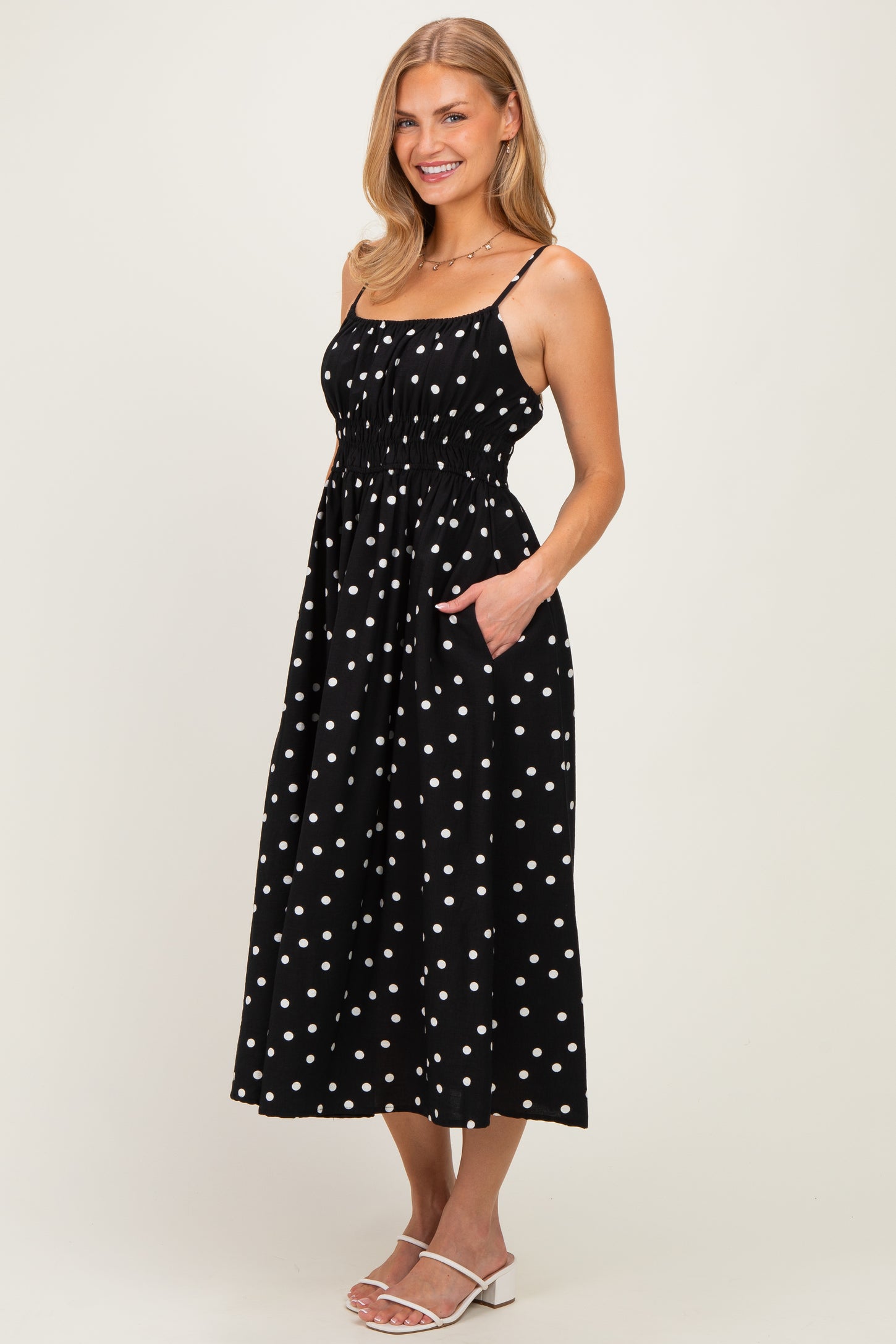 woman wearing a black polka dot midi dress with spaghetti straps and pockets