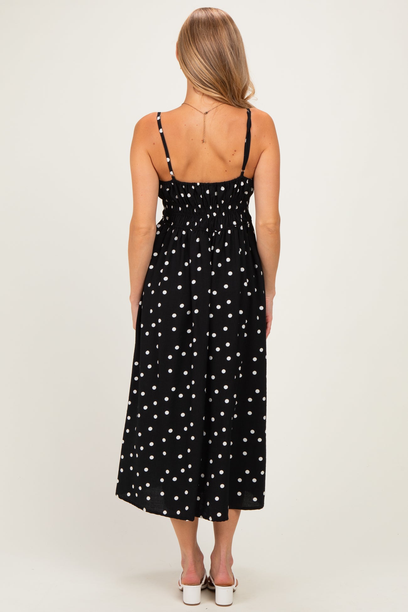 woman wearing a black midi dress with white polka dots and smocked back detail, shown from the back