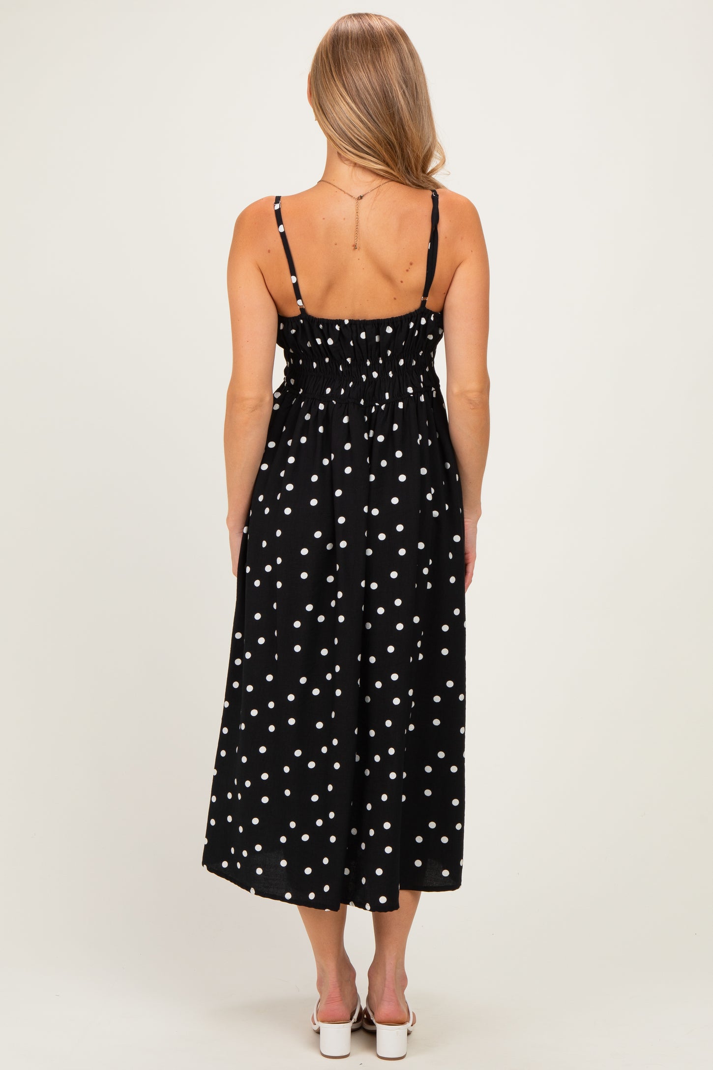 woman wearing a black midi dress with white polka dots and smocked back detail, shown from the back
