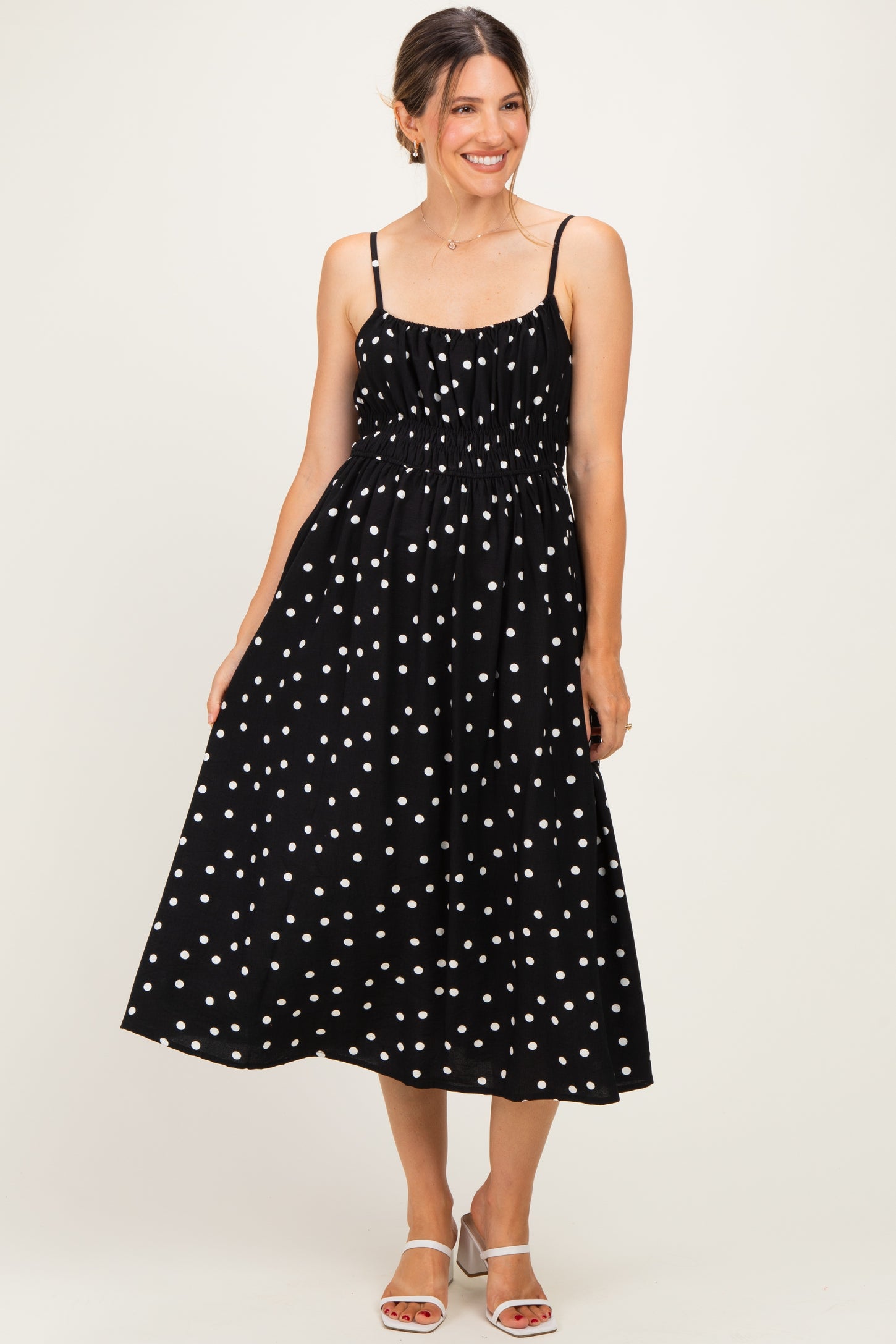 woman wearing a black polka dot maternity dress with smocked bodice and adjustable straps