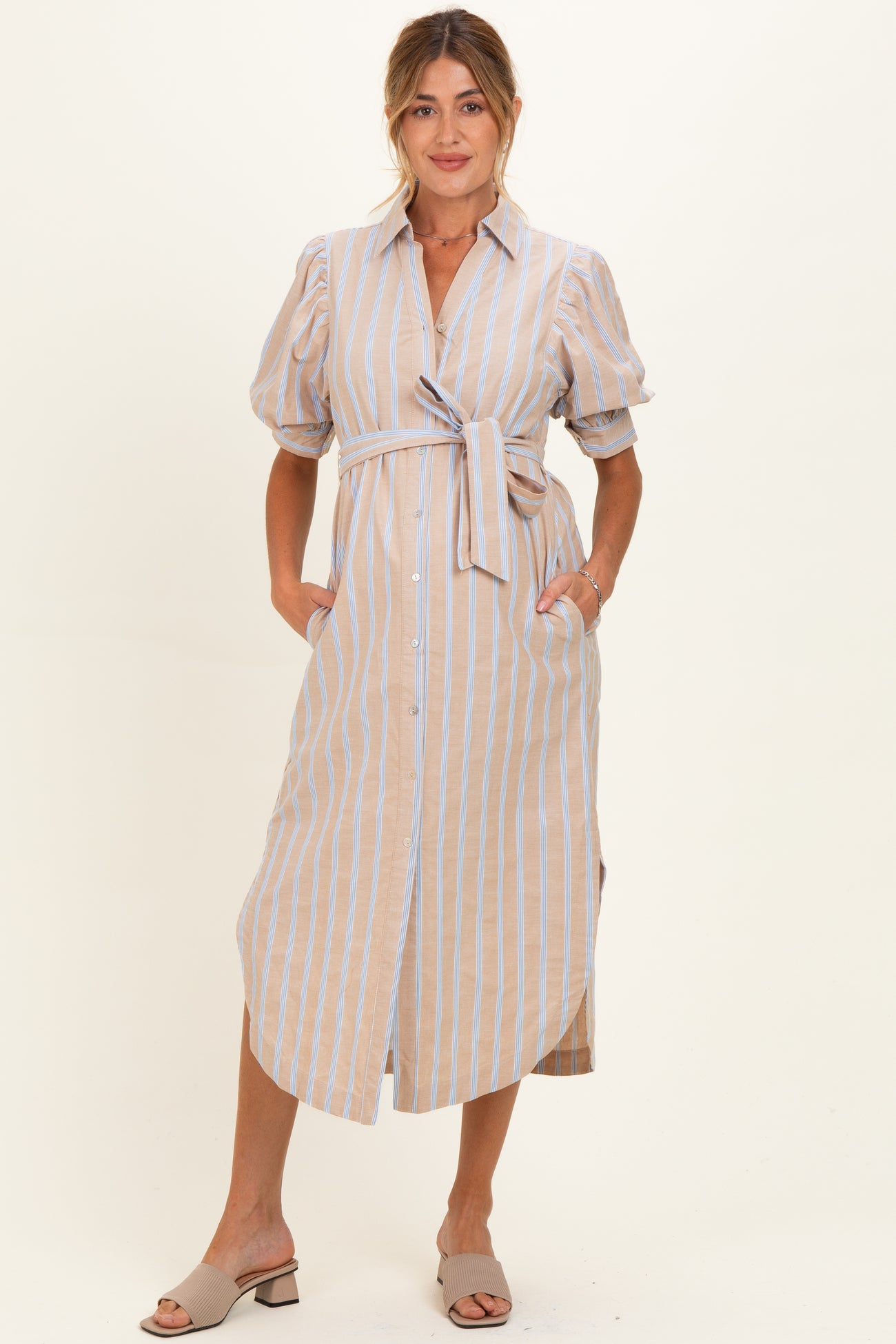 woman wearing a beige and blue striped maternity dress with puff sleeves and a tie waist, holding her baby bump