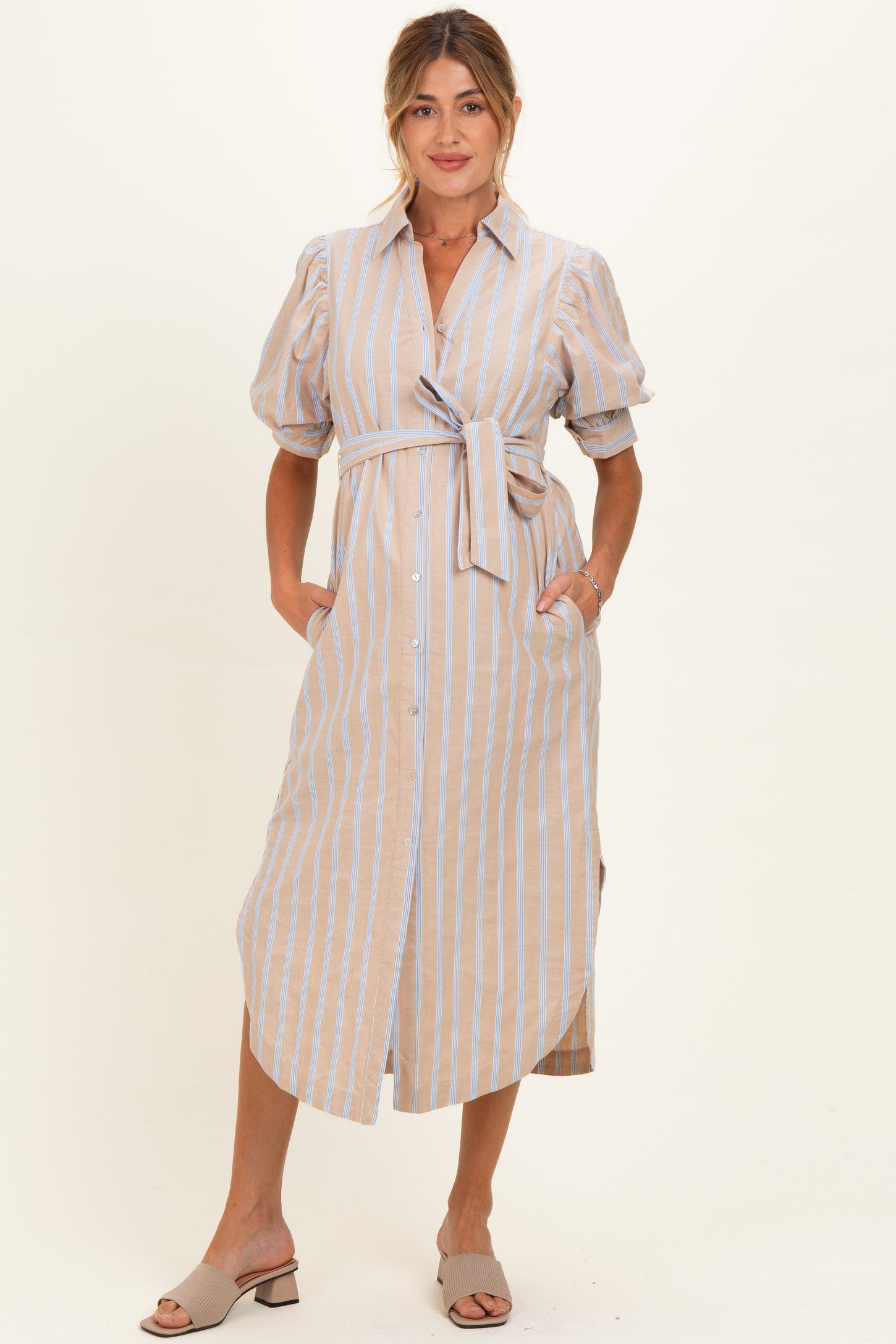 woman wearing a beige and blue striped maternity dress with puff sleeves and a tie waist, holding her baby bump