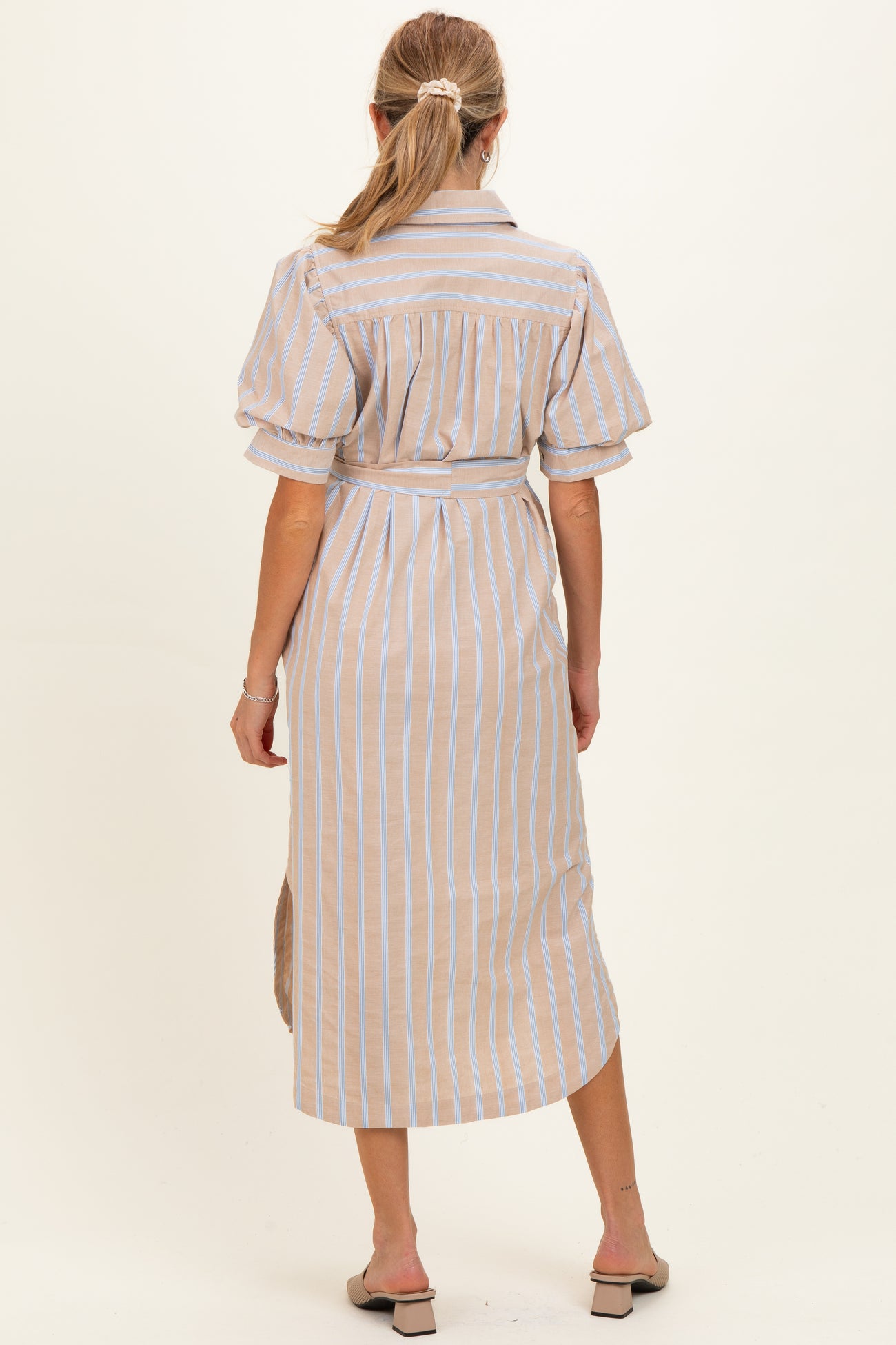 woman wearing a beige and blue striped maternity dress with short puff sleeves, showing a relaxed fit from the back
