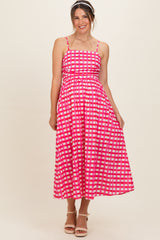 woman wearing a pink checkered maternity maxi dress with spaghetti straps and a fitted bodice, smiling at the camera